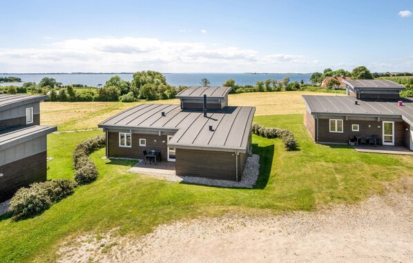 A modern, two-story house with a flat roof, a patio with outdoor furniture, and a view of the water. - Gorgeous home in Faaborg with sauna (Faaborg)