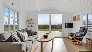 Une pièce spacieuse avec un plafond blanc, une grande fenêtre, un canapé, un fauteuil, une petite table et un téléviseur.