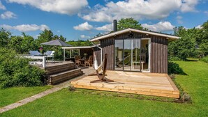 Une maison moderne dotée d’une terrasse en bois, d’un hamac et d’une table de patio.
