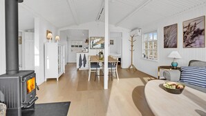 Un vaste espace de vie comprenant un poêle à bois, une table à manger et un coin salon confortable avec des coussins.