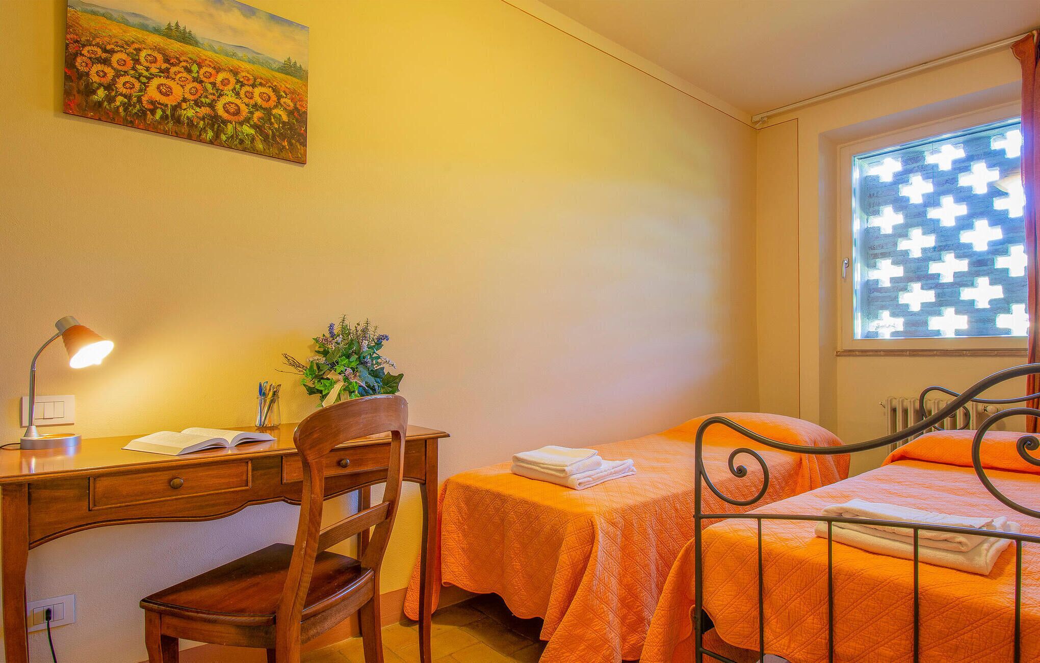 Een slaapkamer met twee bedden, een bureau, een stoel, een lamp en een raam met een gestreept gordijn.