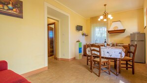 Un coin repas avec une table dressée pour quatre personnes, des chaises en bois, un lustre, un réfrigérateur et une fenêtre laissant entrer la lumière naturelle.