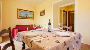 Un coin repas avec une table dressée pour quatre personnes, agrémentée d’une nappe à motifs d’oiseaux, d’une bouteille de vin et de verres à vin vides.