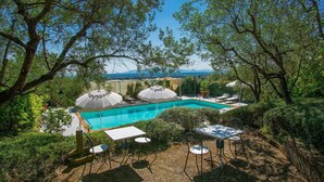 Un espace piscine agrémenté de chaises longues et de parasols, entouré d’arbres et offrant une vue sur le paysage.