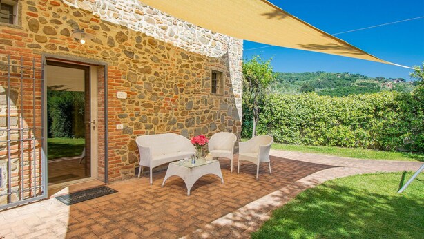 Un bâtiment en pierre doté d’un patio aménagé avec des meubles en osier et une table ornée d’un vase de fleurs.