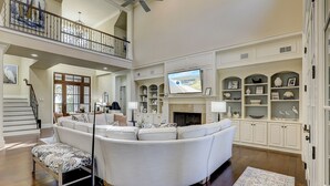 A spacious living room with a high ceiling, a fireplace, and a television mounted above it. - 13 Wagon Rd. Vacation paradise! Close to the beach! Water view! (Hilton Head Island)