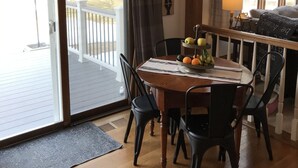 Een eetruimte met een houten tafel, stoelen, een schaal fruit en uitzicht op de omgeving door een schuifdeur.