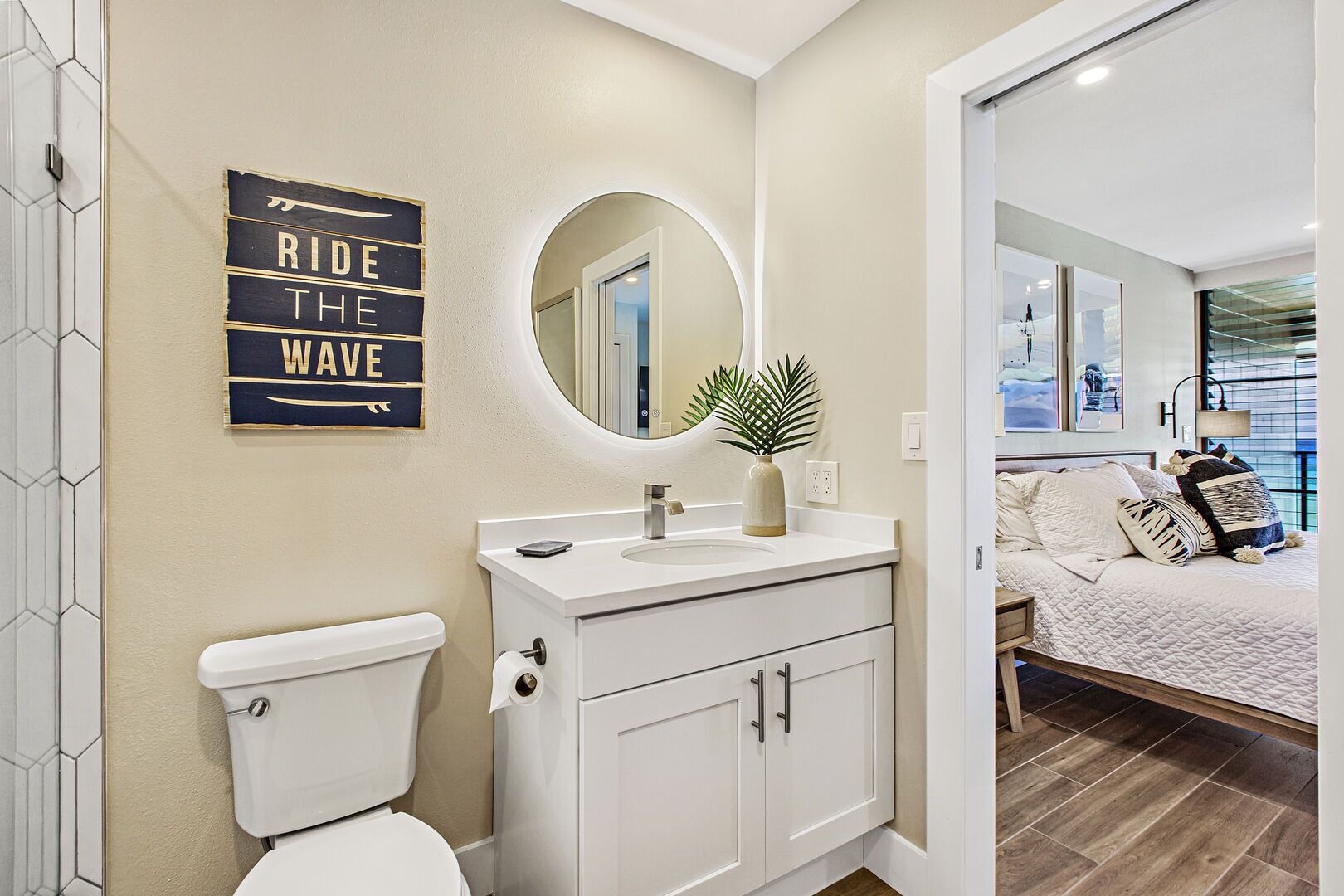 A modern bathroom with a toilet, sink, and vanity. A mirror hangs above the vanity, and a sign on the wall reads "RIDE THE WAVE".