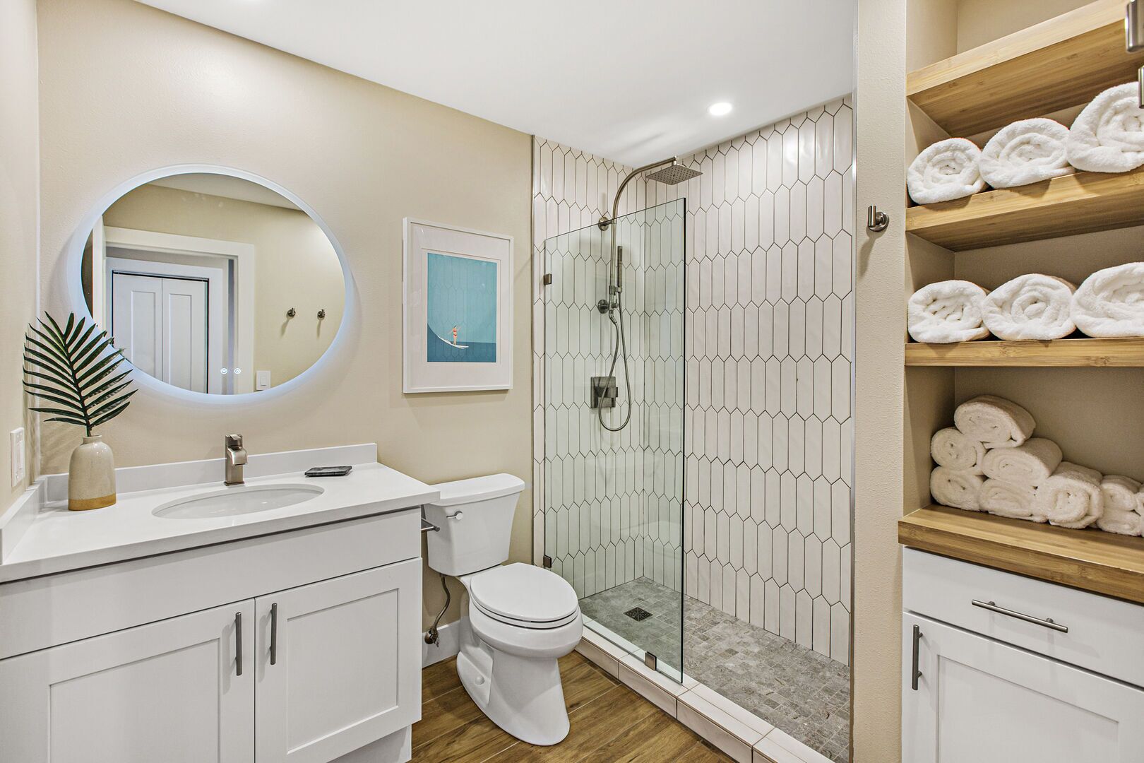 A modern bathroom with a glass-enclosed shower, a toilet, a sink with a mirror, and shelves with rolled towels.