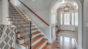 A staircase with wooden steps and metal railings, leading to a hallway with a white door and a chandelier. - Luxury North Beach Resort home w/ private pool, master on main & open floor plan (North Myrtle Beach)