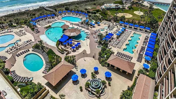 An aerial view of a resort with multiple swimming pools, sun loungers, and a beach area. - Luxury North Beach Resort home w/ private pool, master on main & open floor plan (North Myrtle Beach)