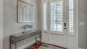 A hallway with a glass-top console table, a framed artwork, and a double door with a window. - Luxury North Beach Resort home w/ private pool, master on main & open floor plan (North Myrtle Beach)