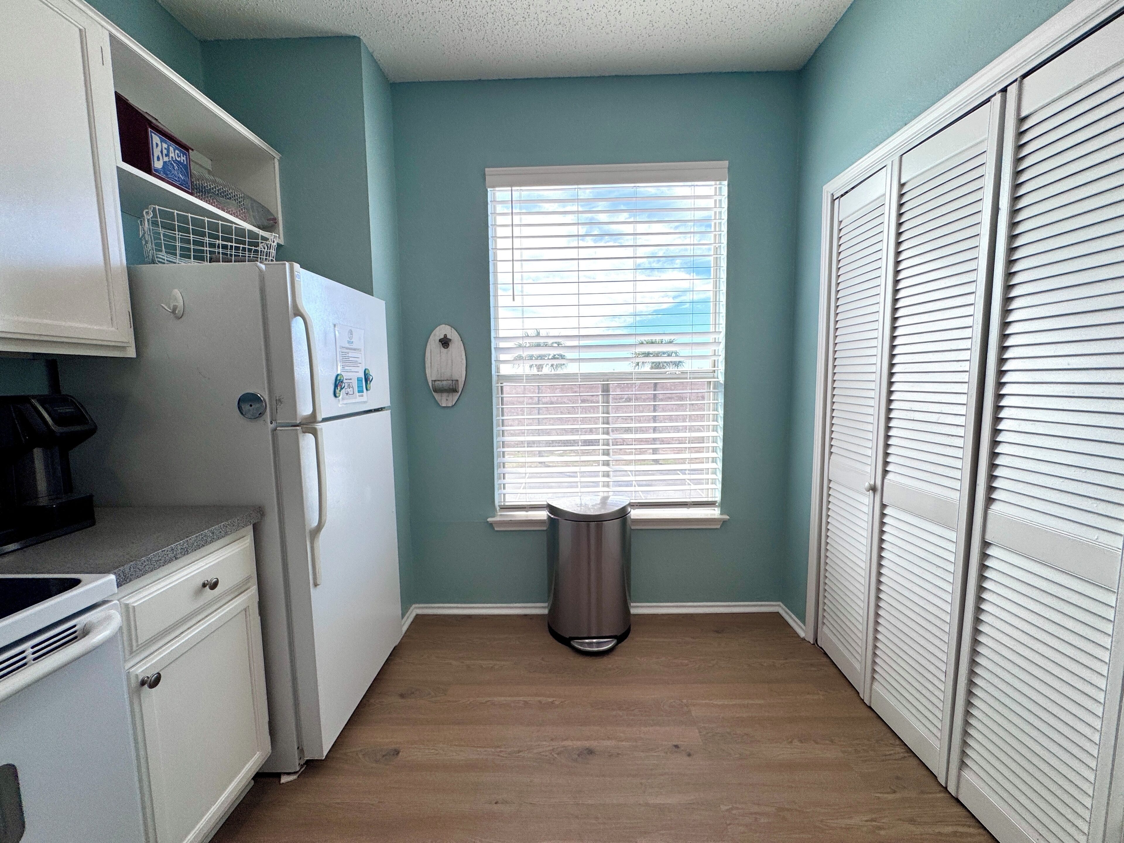 A kitchen with a refrigerator, a coffee maker, and a trash can.