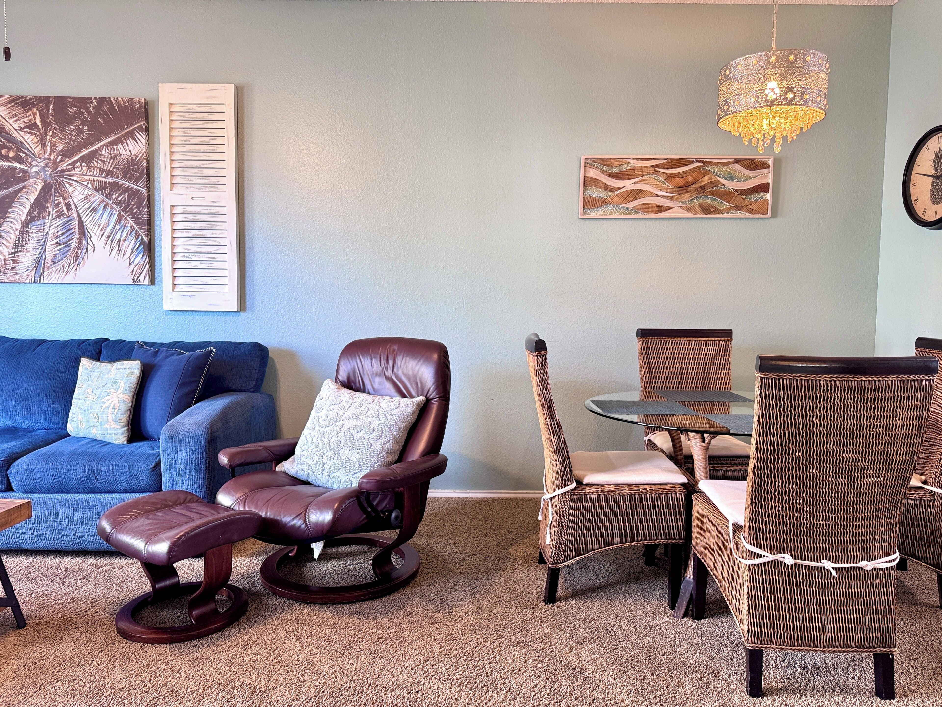 A living room with a blue sofa, a brown leather chair, wicker chairs, a glass table, and a chandelier.