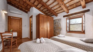Une chambre avec deux lits, des meubles en bois, un mur en pierre et une fenêtre.