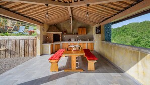 Un espace cuisine extérieur doté d’un four en pierre, de meubles en bois et d’une table à manger avec des bancs.
