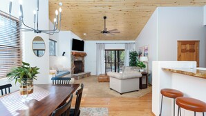 Een moderne keuken met een houten plafond, een eetgedeelte met een houten tafel en stoelen, en een woonkamer met een bank en een open haard.