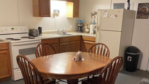 Una cocina con armarios de madera, una estufa blanca, un lavamanos y una mesa de comedor con sillas.