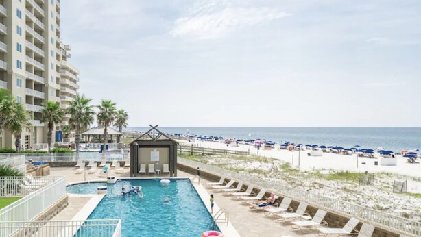 Un espace piscine avec des chaises longues et vue sur la plage.