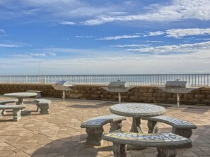 Outdoor seating with mosaic-tiled tables and benches, a stone wall, and a view of the sea. - 6th Floor Gulf Front Corner - 3 bedrooms, 3 baths (Orange Beach)