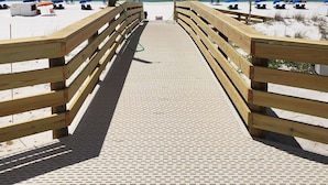Une promenade en bois menant à une plage où se trouvent des parasols bleus et un drapeau.