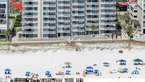 Un hôtel à plusieurs étages doté de balcons, avec une plage en premier plan et un espace piscine.