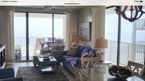 Un salon spacieux avec un grand canapé, une table basse et une table à manger. Il y a un balcon avec vue sur l’océan.