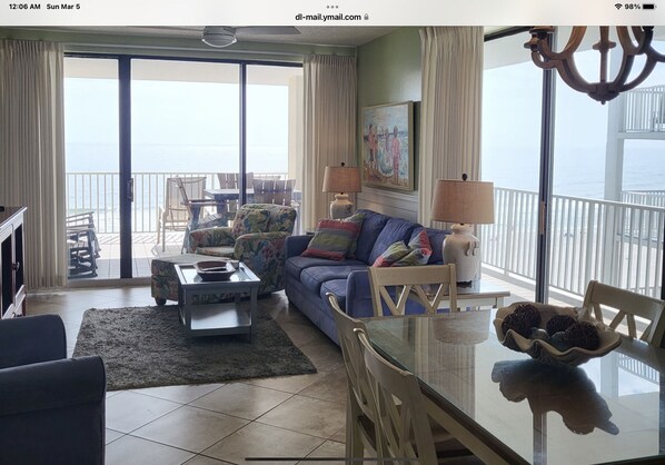 Un salon spacieux avec un grand canapé, une table basse et une table à manger. Il y a un balcon avec vue sur l’océan.