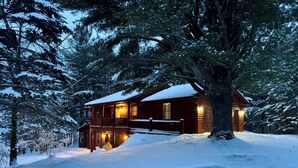 A wooden cabin with a balcony, surrounded by snow-covered trees. - 30 acres, steam sauna, hot tub, 7 beds, sleeps 10. We LOVE dogs! (Onekama)