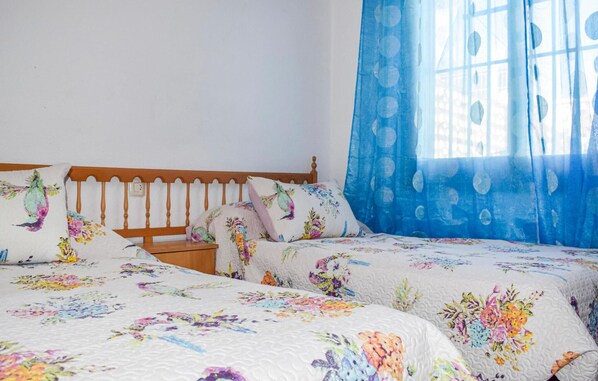 A bedroom with two beds, wooden headboards, floral bedding, and a window with blue curtains. - Gorgeous home in Los Alcázares with WiFi (Los Alcázares)