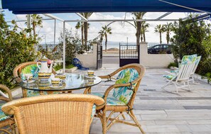 An outdoor patio with wicker furniture, a glass table, and a view of the beach and mountains. - Gorgeous home in Los Alcázares with WiFi (Los Alcázares)