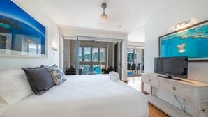 Ett modernt hotellrum med en stor säng, en platt-TV, en tavla som föreställer ett blått hav och utsikt över utomhusområdet.