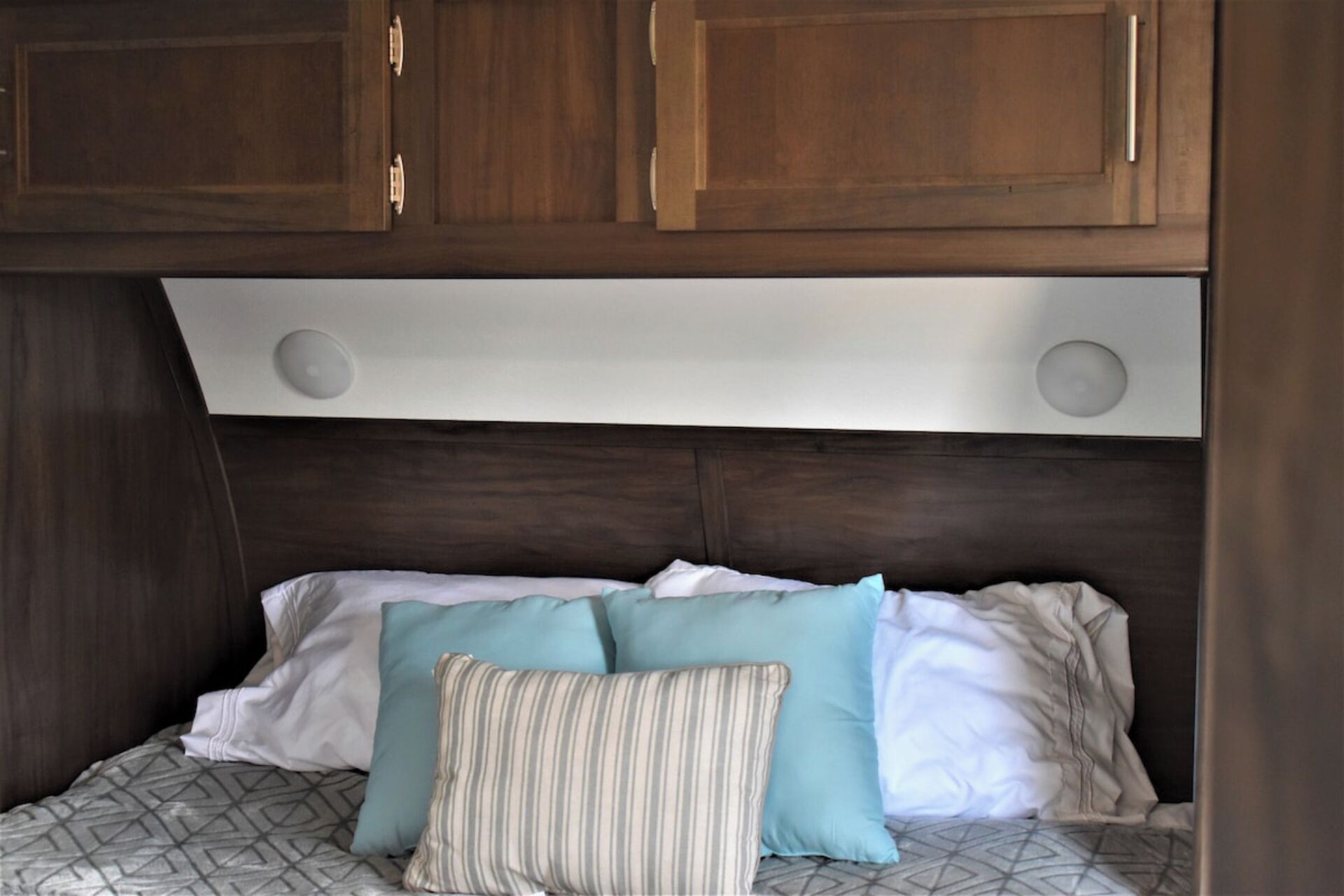 A bed with a geometric patterned bedspread, two pillows, and a headboard with a built-in shelf.