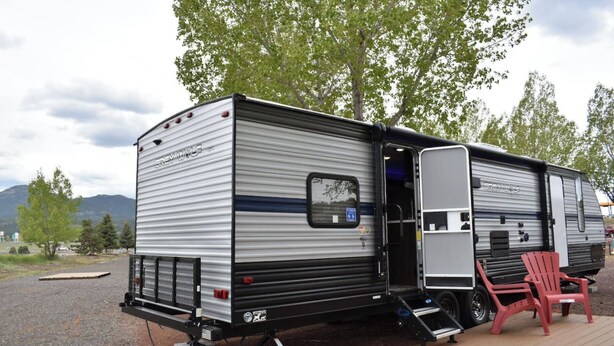 A grey and black RV with a sliding door, a small attached structure, and a red chair on a wooden deck. - Grand Canyon RV Glamping Premium Suite #2 (Glamping Getaway) (Williams)