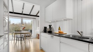 Een moderne keuken met witte kasten, een zwart aanrecht en een eethoek van hout met uitzicht op de omgeving.