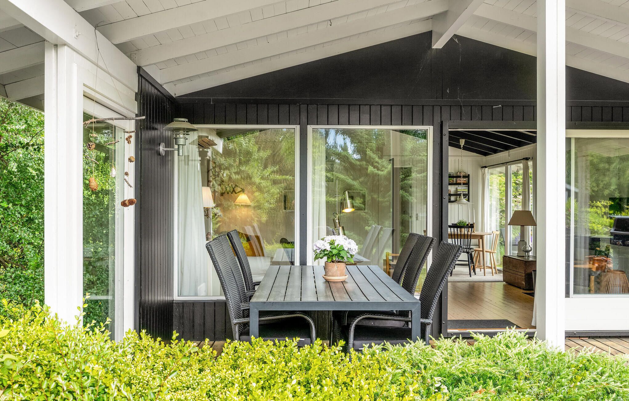 An outdoor dining area with a table and chairs, surrounded by glass walls and a wooden deck.