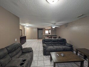A living room with a sofa, a coffee table, and a dining area in the background.