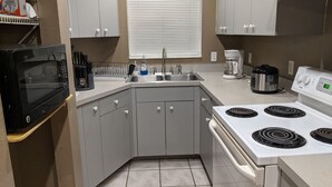 A compact kitchen with a microwave, stove, sink, and a window with blinds. - Snowbirds escape / vacation gateway (Englewood)