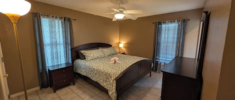 Un dormitorio con cama, mesitas de noche, ventilador de techo y cómoda.