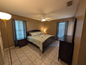Quarto com cama, mesas de cabeceira, ventoinha no teto e cômoda.