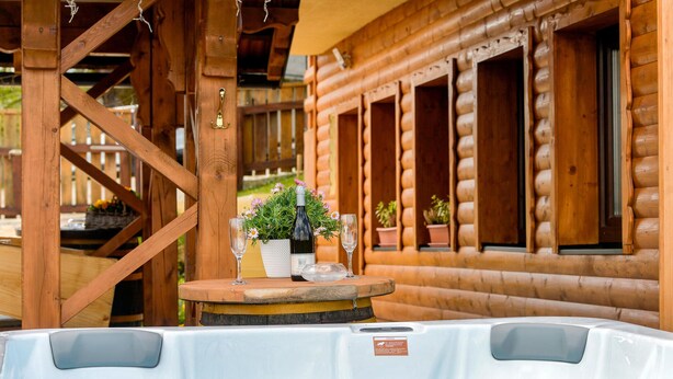 Une cabane en bois avec un jacuzzi au premier plan et une fenêtre ornée d’une plante en pot sur la droite.