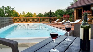 Une scène au bord de la piscine, avec deux verres de vin rouge posés sur une table, une bouteille de vin et des chaises longues.