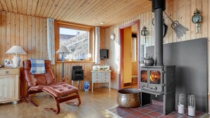 L’intérieur chaleureux d’un chalet, avec un décor en bois, une cheminée, un fauteuil en cuir, une petite table et une fenêtre donnant sur la forêt.