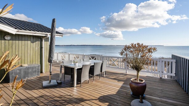 Une terrasse en bois avec une table et des chaises, donnant sur une étendue d’eau.
