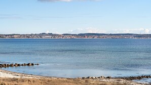 Une vue sur la côte, avec une mer calme, un rivage rocheux et, au loin, une ville avec ses bâtiments et une colline.
