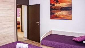 A hotel room with two beds, a door leading to another room, and a sunset painting on the wall. - Gorgeous apartment in Grebastica with WiFi (Grebastica)