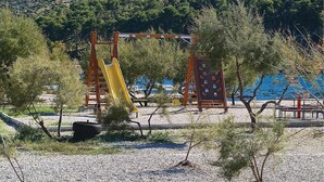 A playground with a yellow slide and climbing structures, surrounded by trees and a body of water in the background. - Gorgeous apartment in Grebastica with WiFi (Grebastica)