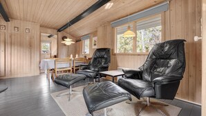Un interior moderno con paredes de madera, una zona de comedor con mesa y sillas, y un espacio de estar con sofá y sillón.