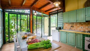 A kitchen with a wooden table, green cabinets, and a view of greenery through large windows. - Lovely home in Scicli (Scicli)