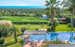 Un espace piscine offrant une vue sur la mer, entouré d’une végétation luxuriante et de palmiers.